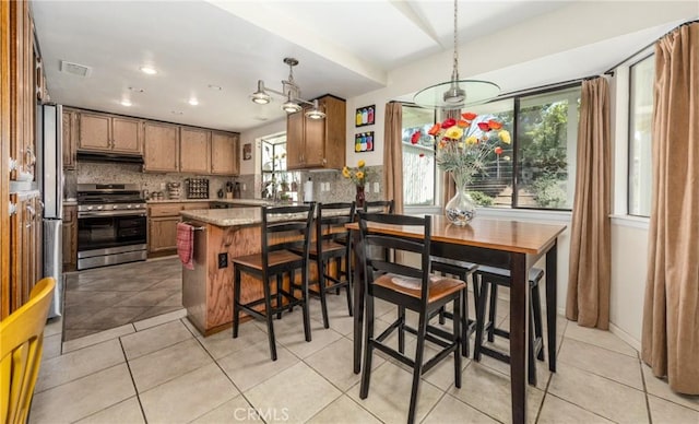 kitchen with tasteful backsplash, a peninsula, light tile patterned floors, brown cabinetry, and stainless steel gas stove