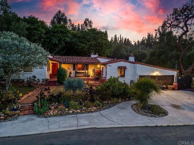 mediterranean / spanish-style house with a garage, stucco siding, driveway, and a chimney