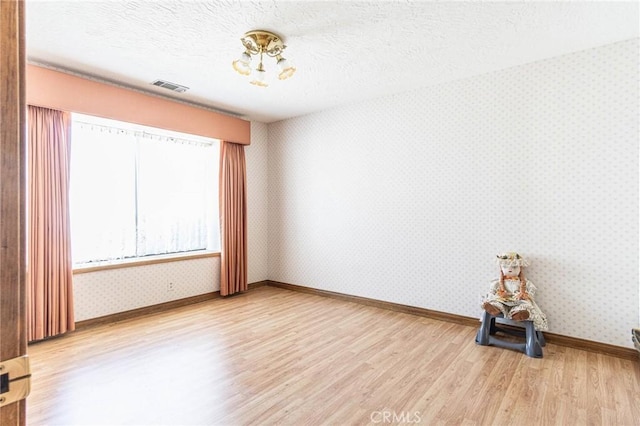7040 Kenyon Ave, Hesperia, CA 92345 - unfurnished room with baseboards, wallpapered walls, a textured ceiling, visible vents, and wood finished floors