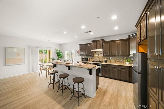73992 Van Gogh Dr, Palm Desert, CA 92211 - kitchen featuring appliances with stainless steel finishes, under cabinet range hood, a kitchen bar, dark brown cabinets, and light wood-style flooring
