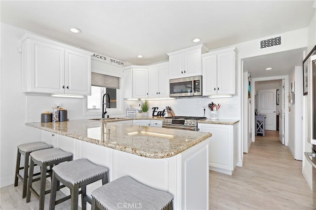 kitchen featuring stainless steel appliances, visible vents, a sink, a breakfast bar area, and white cabinetry