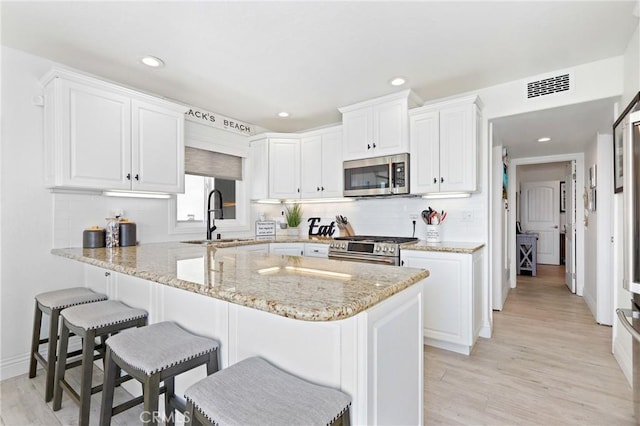 916 E Oceanfront, Newport Beach, CA 92661 - kitchen with appliances with stainless steel finishes, a kitchen breakfast bar, white cabinets, light stone countertops, and recessed lighting