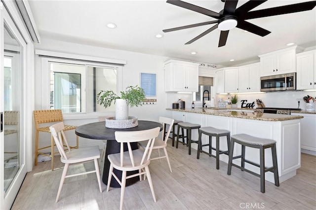 kitchen featuring stainless steel microwave, a wealth of natural light, white cabinets, and a breakfast bar