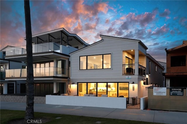 916 E Oceanfront, Newport Beach, CA 92661 - back of property at dusk featuring a balcony, a fenced front yard, and a gate