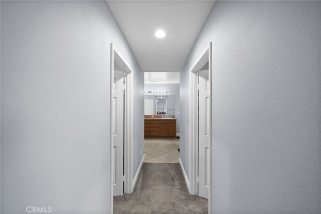 hallway with baseboards and light colored carpet