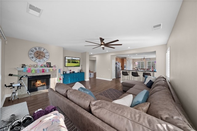 living room with visible vents, a fireplace with flush hearth, dark wood finished floors, and a ceiling fan