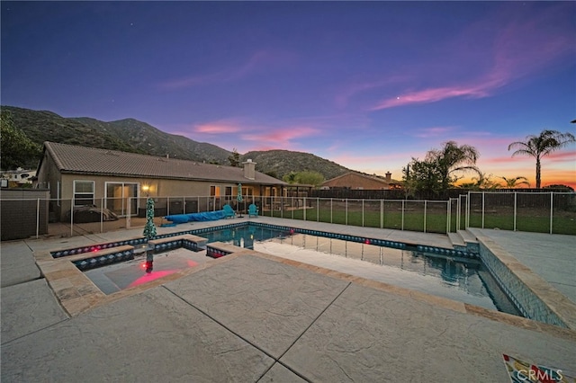 pool at dusk featuring a fenced backyard, a patio, a mountain view, and a pool with connected hot tub