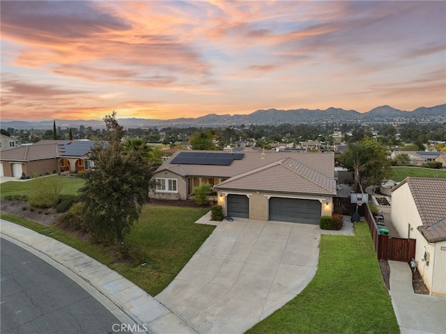 view of front facade featuring an attached garage, a mountain view, a lawn, a tiled roof, and driveway