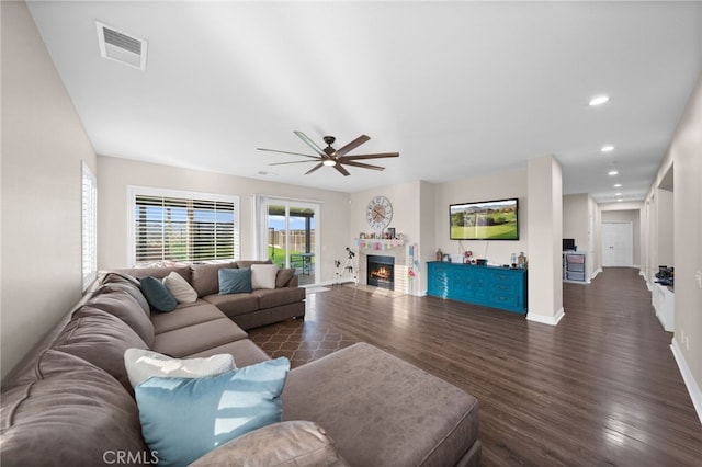 living room featuring a ceiling fan, a lit fireplace, visible vents, dark wood finished floors, and baseboards