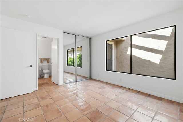 unfurnished bedroom featuring a closet, light tile patterned flooring, ensuite bath, and baseboards