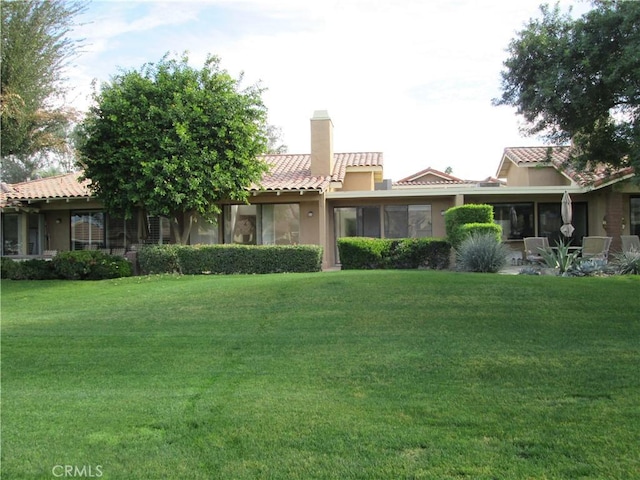 view of front of property with a tiled roof, a chimney, a front lawn, and stucco siding