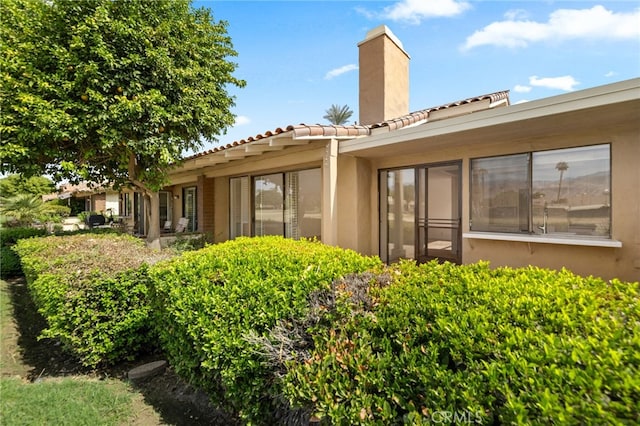 rear view of property featuring a chimney, a tile roof, and stucco siding