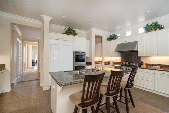 2927 Rancho Cortes, Carlsbad, CA 92009 - kitchen with under cabinet range hood, a sink, backsplash, a kitchen island with sink, and a kitchen breakfast bar