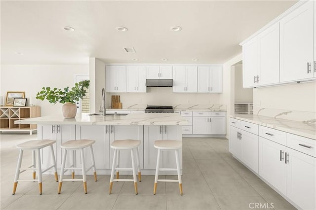 19201 Barrett Ln, North Tustin, CA 92705 - kitchen featuring under cabinet range hood, white cabinetry, a breakfast bar, a kitchen island with sink, and stove
