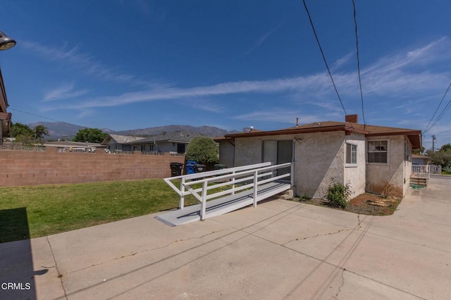 exterior space featuring a lawn, fence, a mountain view, a patio, and stucco siding