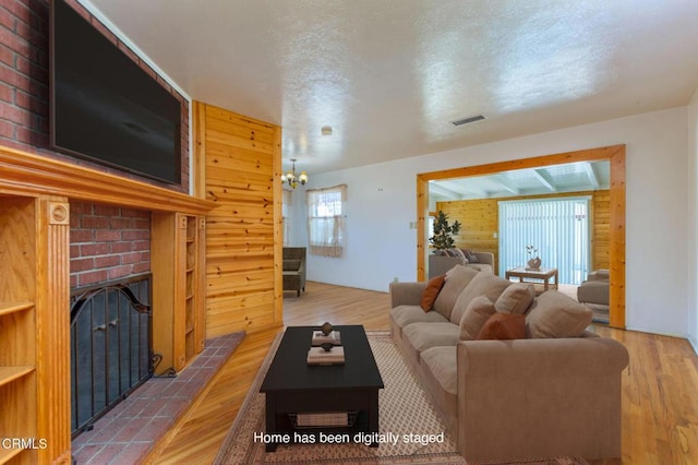 living area featuring an inviting chandelier, a brick fireplace, wood walls, wood finished floors, and visible vents