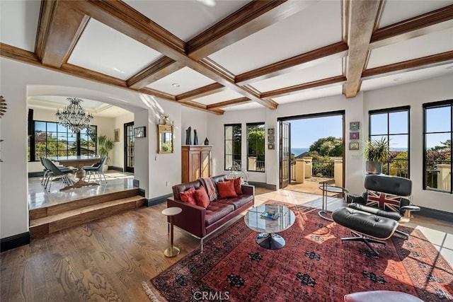 living room featuring a chandelier, arched walkways, coffered ceiling, and a healthy amount of sunlight