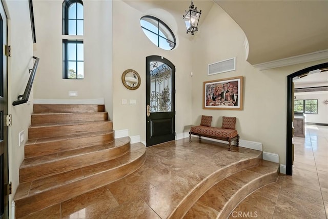 foyer entrance with a towering ceiling, baseboards, stairs, visible vents, and arched walkways