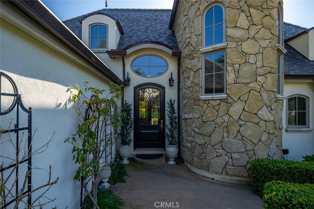 property entrance featuring roof with shingles, stucco siding, and stone siding