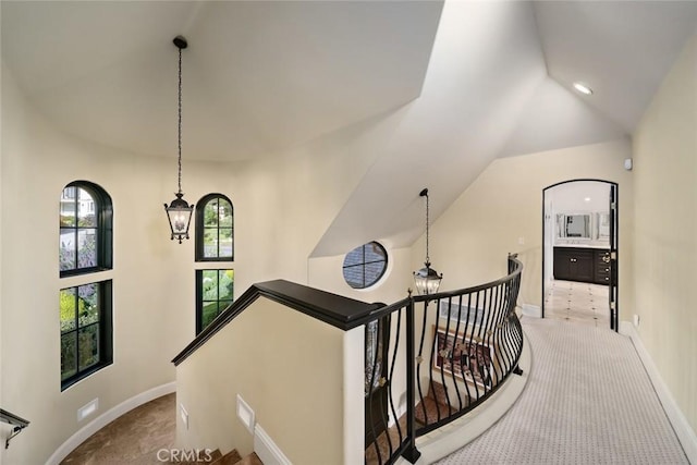 hall with carpet, baseboards, vaulted ceiling, and an upstairs landing