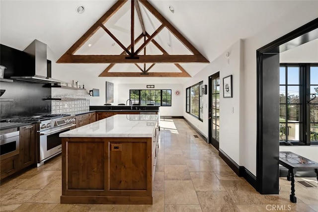 kitchen with wall chimney exhaust hood, light stone countertops, high end stove, stone finish flooring, and a kitchen island