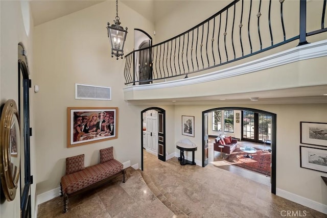 foyer entrance with arched walkways, a towering ceiling, visible vents, baseboards, and a notable chandelier