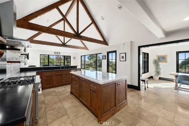 kitchen featuring beamed ceiling, stainless steel range with gas stovetop, a center island, and wall chimney exhaust hood