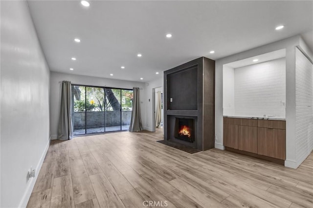 unfurnished living room with light wood-style flooring, a large fireplace, baseboards, and recessed lighting