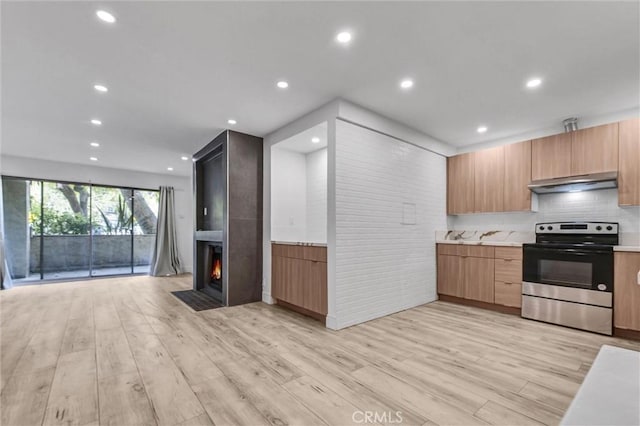 kitchen with open floor plan, light countertops, stainless steel range with electric stovetop, under cabinet range hood, and light wood-style floors