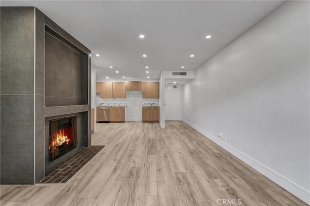unfurnished living room with baseboards, recessed lighting, a fireplace, visible vents, and light wood finished floors
