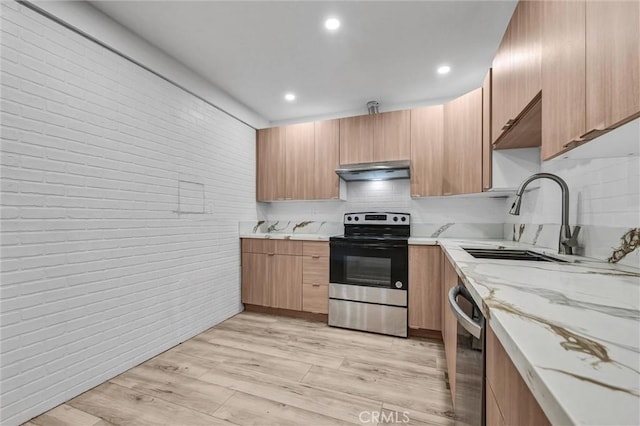 kitchen with under cabinet range hood, light stone counters, a sink, stainless steel appliances, and brick wall