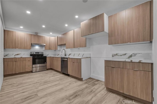 kitchen featuring a sink, light countertops, under cabinet range hood, stainless steel appliances, and backsplash