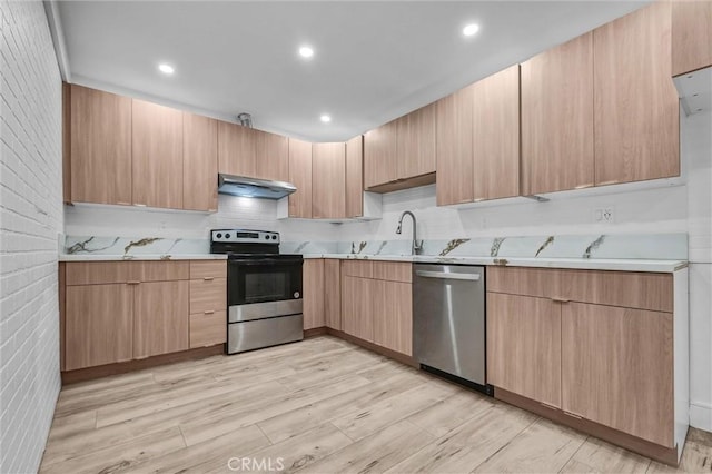 kitchen with a sink, light wood-type flooring, appliances with stainless steel finishes, light brown cabinetry, and under cabinet range hood