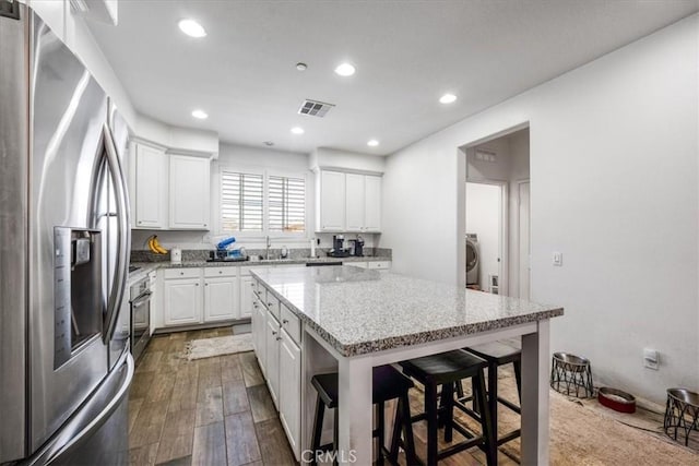 40925 Lacroix Ave, Murrieta, CA 92562 - kitchen featuring white cabinetry, stainless steel refrigerator with ice dispenser, washer / dryer, visible vents, and a breakfast bar area