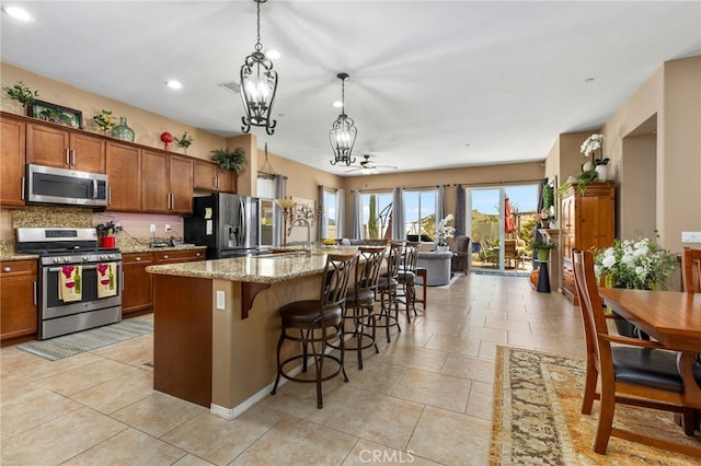 kitchen with brown cabinets, appliances with stainless steel finishes, a notable chandelier, and light stone counters