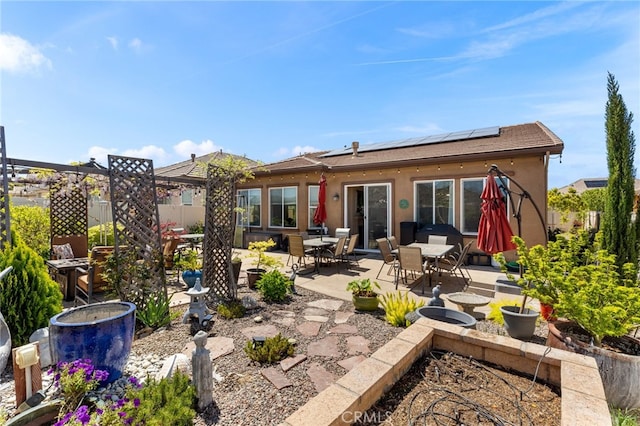 back of house with roof mounted solar panels, outdoor dining space, fence, a patio, and stucco siding