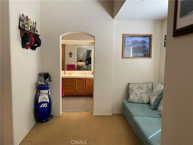 hall featuring light carpet, arched walkways, baseboards, and a sink