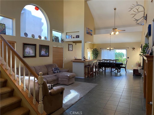 living room featuring high vaulted ceiling, dark tile patterned floors, stairway, and ceiling fan with notable chandelier