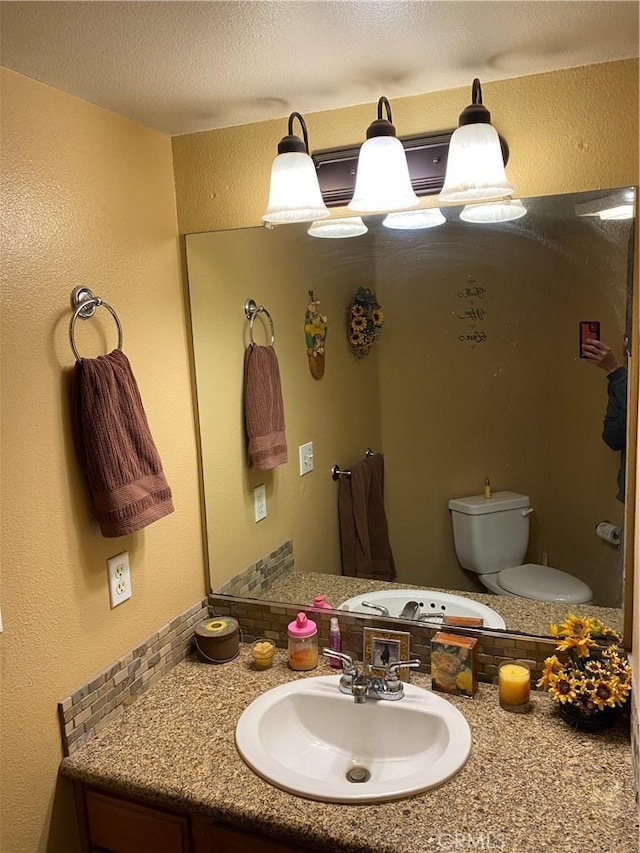 bathroom featuring toilet, a textured ceiling, vanity, and a textured wall