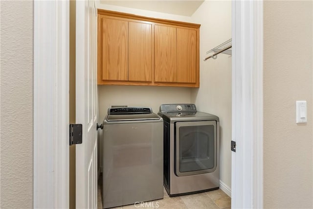 clothes washing area featuring cabinet space, washer and clothes dryer, and light tile patterned floors