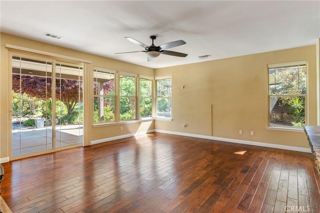 empty room with wood finished floors, ceiling fan, baseboards, and visible vents