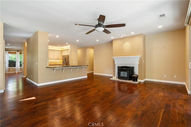 unfurnished living room featuring dark wood-style floors, a sink, baseboards, visible vents, and ceiling fan