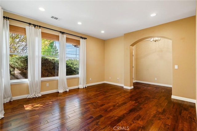 unfurnished room featuring baseboards, hardwood / wood-style flooring, visible vents, and arched walkways