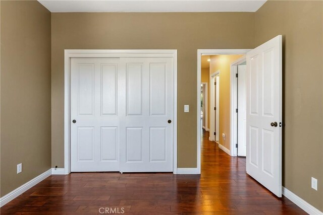 unfurnished bedroom with baseboards, a closet, and dark wood finished floors