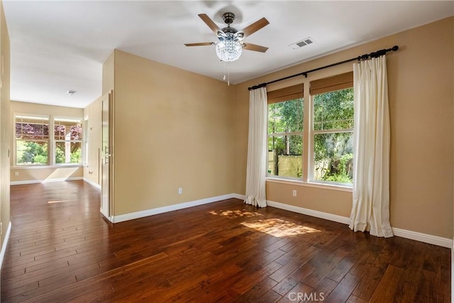 spare room with dark wood-style flooring, visible vents, ceiling fan, and baseboards