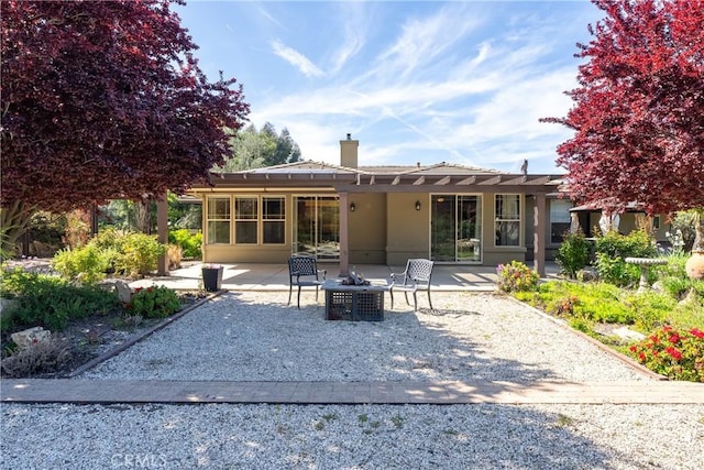 back of house with a chimney, a pergola, stucco siding, a patio area, and an outdoor fire pit
