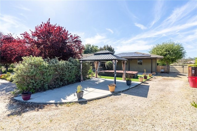rear view of house with a gazebo, a patio area, roof mounted solar panels, fence, and stucco siding