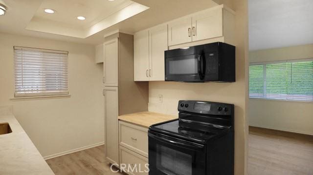 kitchen with light countertops, light wood-style flooring, white cabinets, and black appliances
