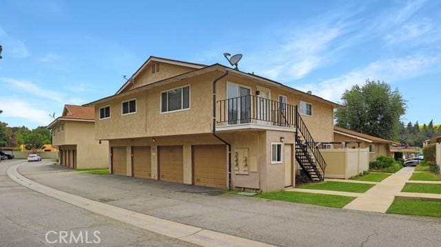 view of side of property with aphalt driveway, a garage, stairs, a balcony, and stucco siding