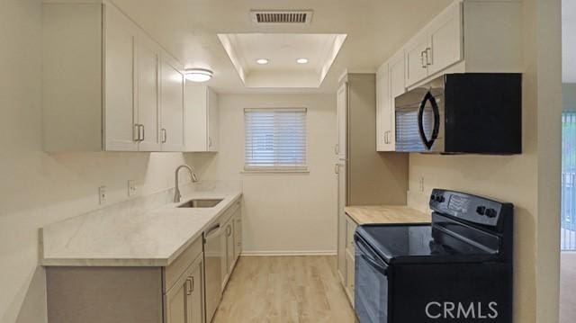 kitchen with a sink, black appliances, a tray ceiling, light countertops, and visible vents